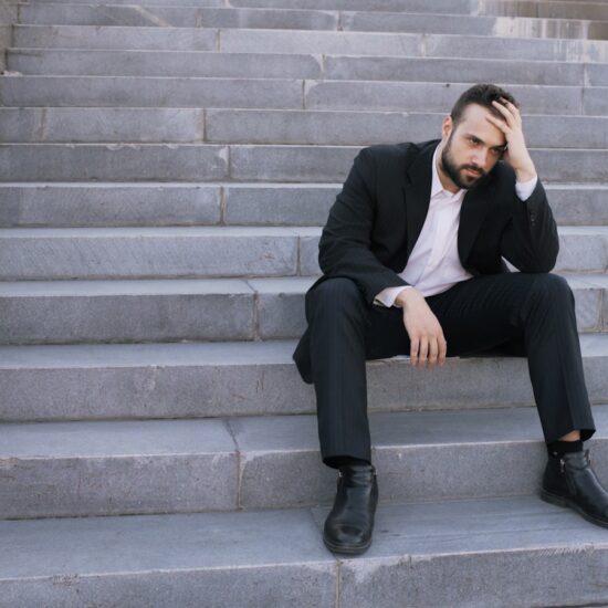 Upset young business man having stress and sitting on stairs in street. Businessman having deal problems at work concept