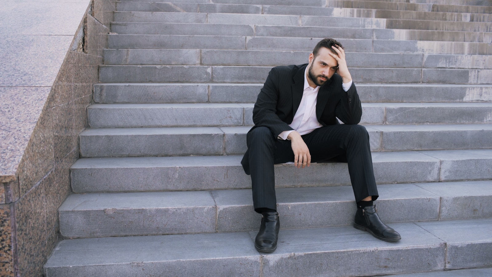 Upset young business man having stress and sitting on stairs in street. Businessman having deal problems at work concept